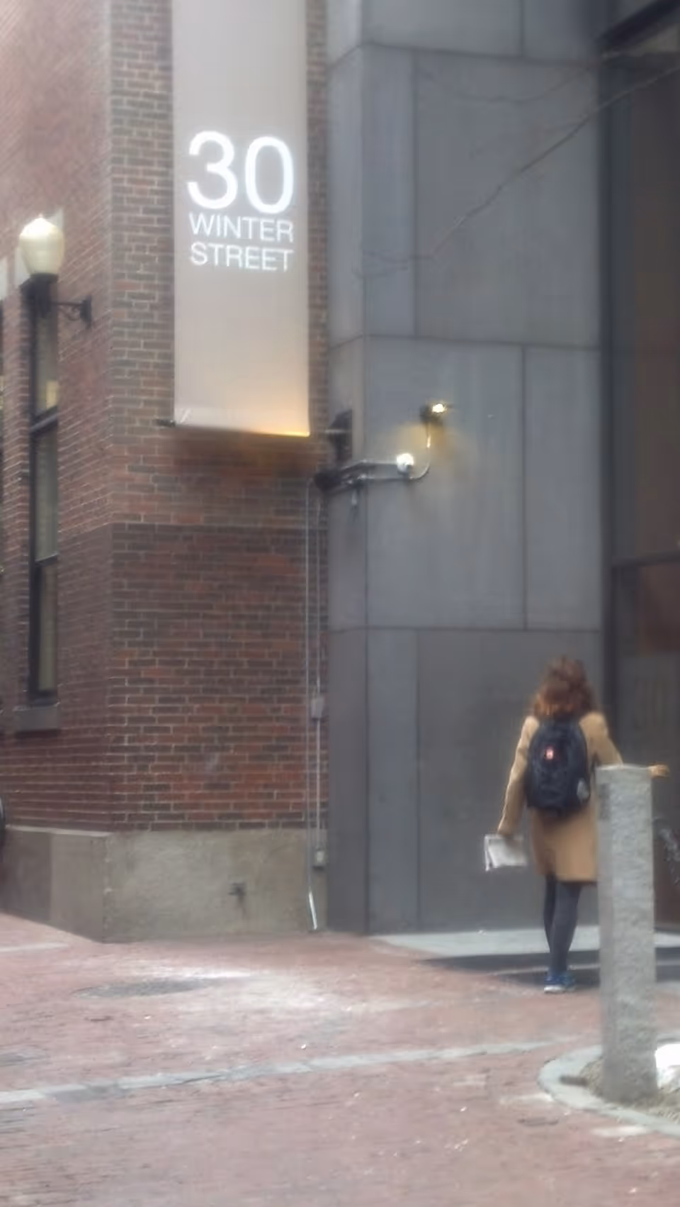 A person walking on a brick street beside a building with a 30 Winter Street sign.