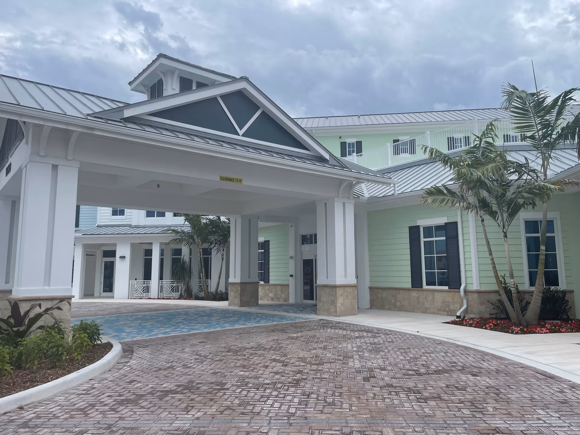 Front view of a light-colored senior living facility with a covered entrance and palm trees.