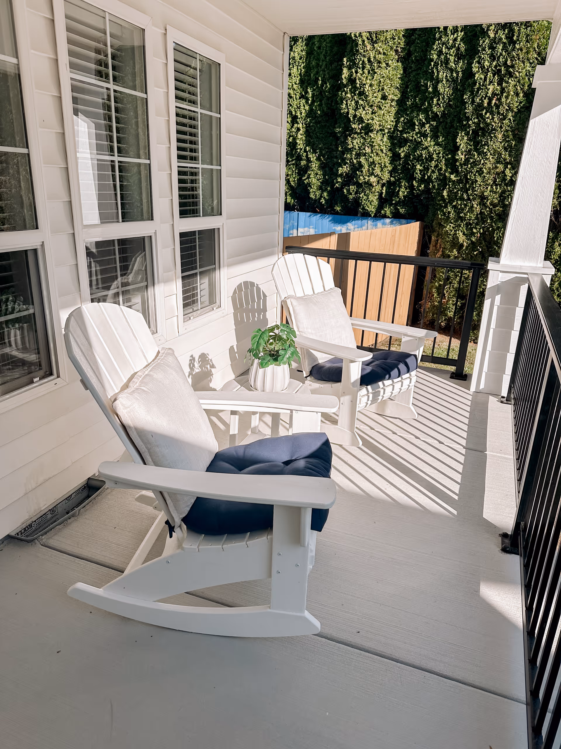 White outdoor balcony with two Adirondack chairs and a potted plant.