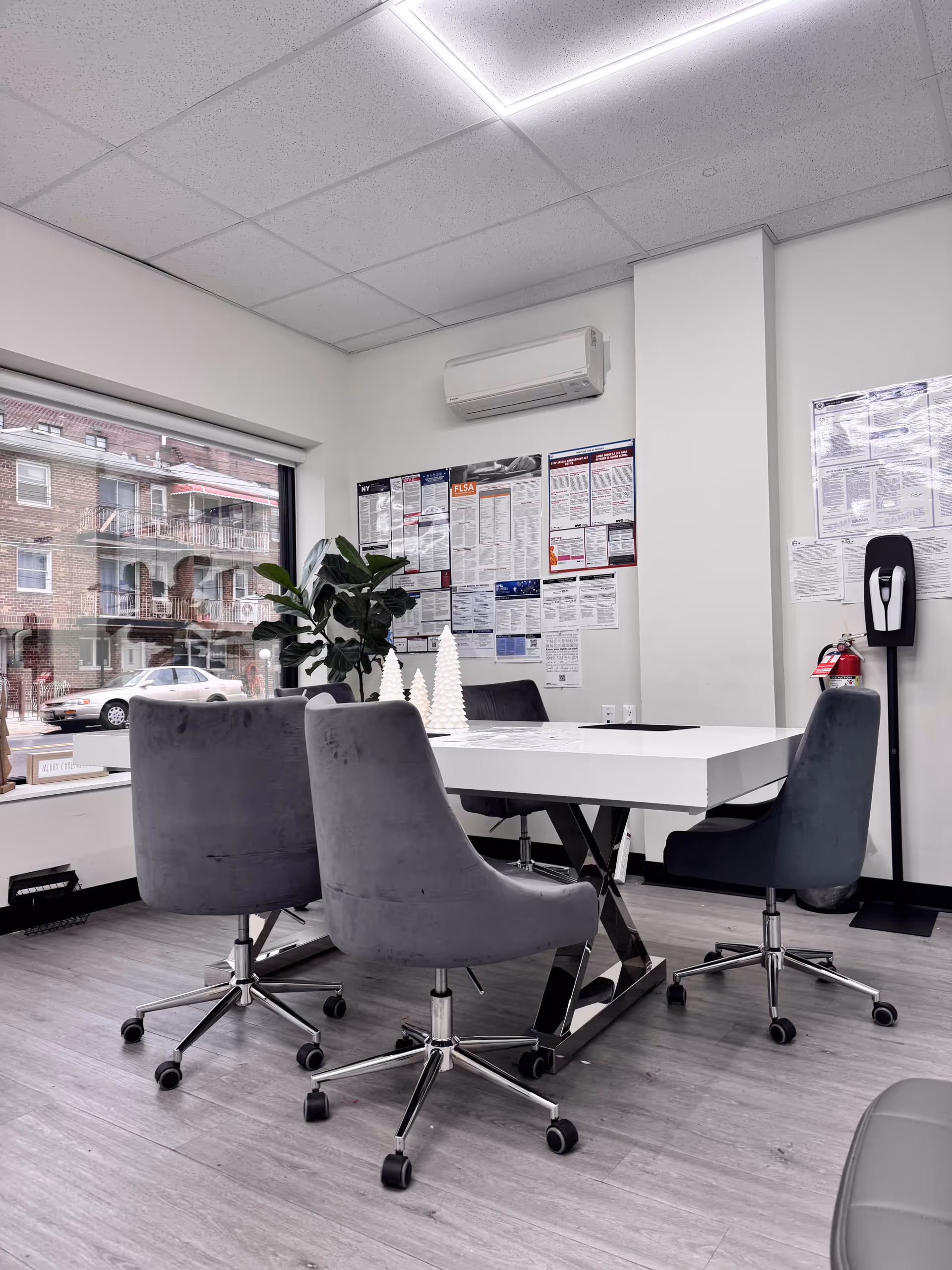 Modern office-style room with a white table, gray swivel chairs, posters, and a window view.