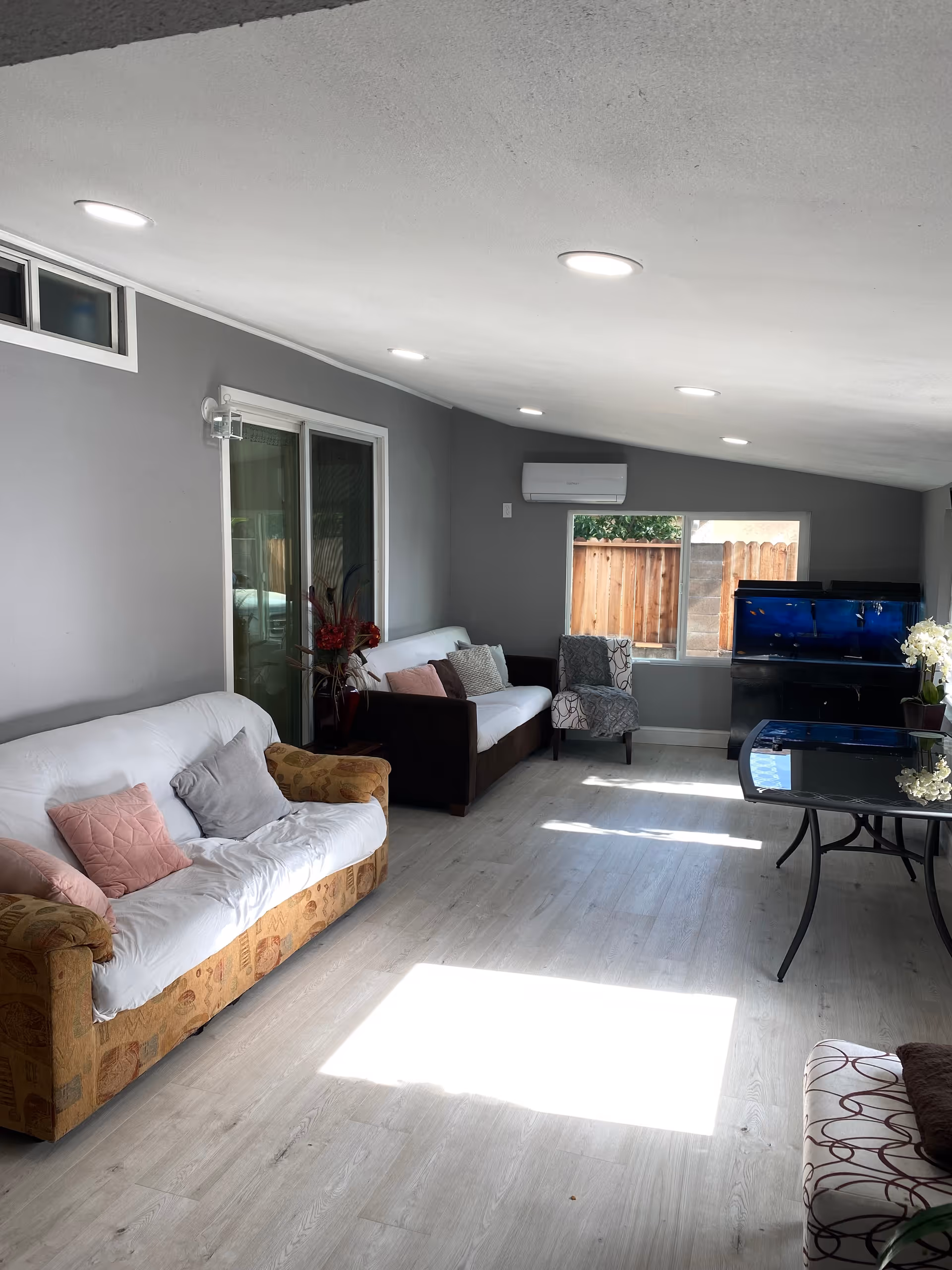 Bright living room in a gray facility with couches, chairs, aquarium, and glass table.