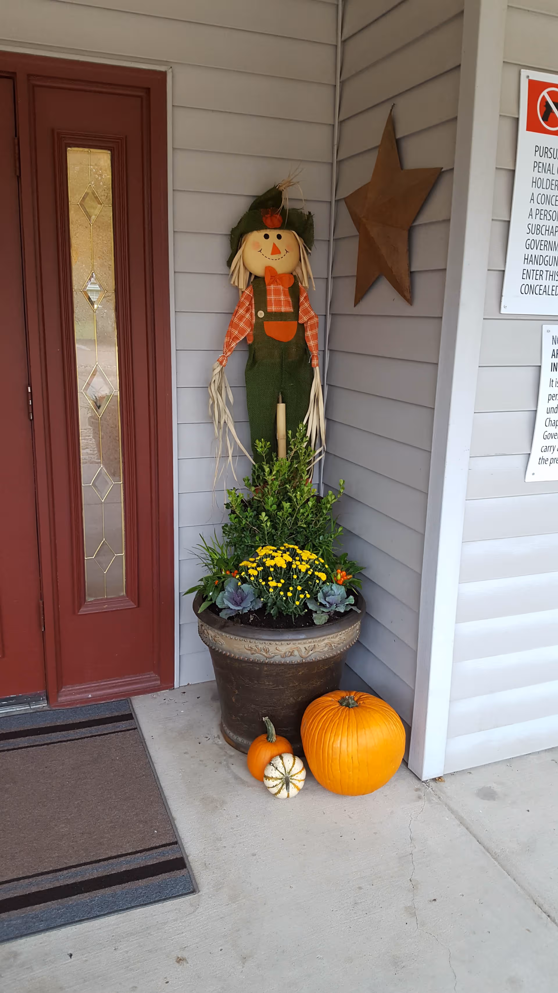 A front entry porch of Cleburne Court with pumpkins, a scarecrow, potted plants, and seasonal decoration.