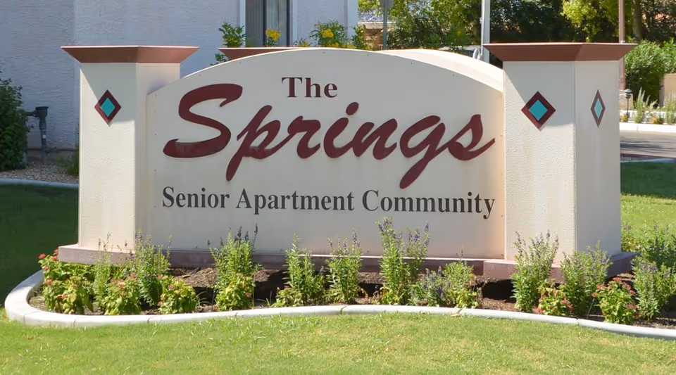 A large curved sign reading The Springs Senior Apartment Community with landscaped garden in front