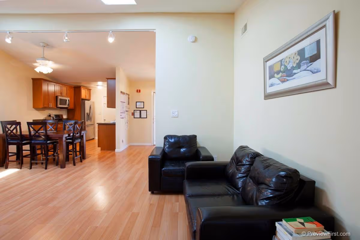 Open-concept living area with black leather sofas, dining table, and kitchen in background.