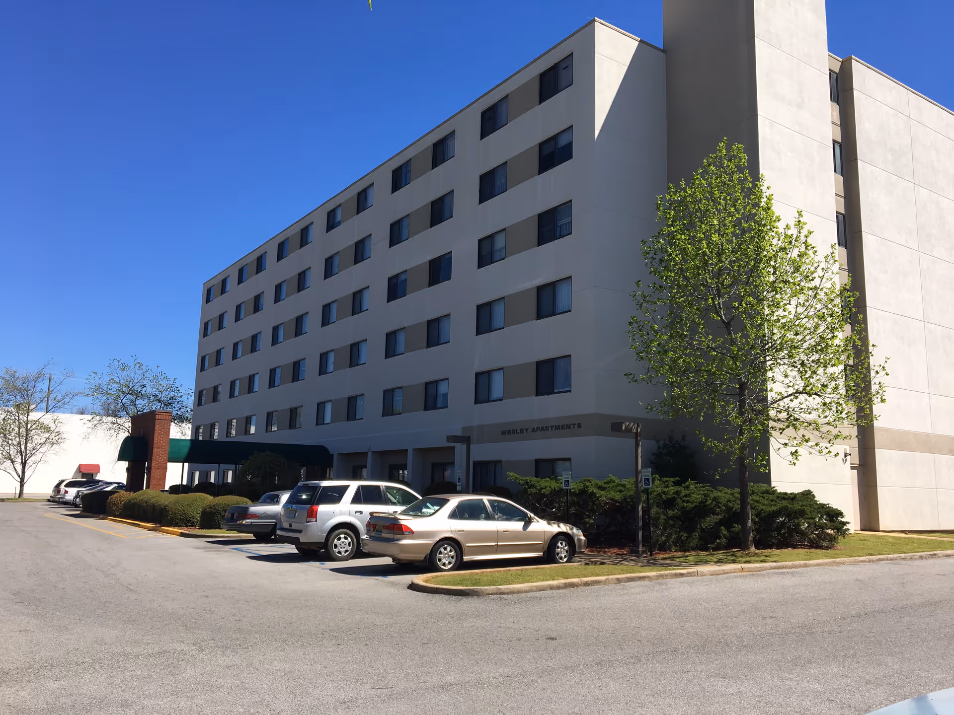 Exterior of Wesley Apartments senior living building with parked cars and blue sky