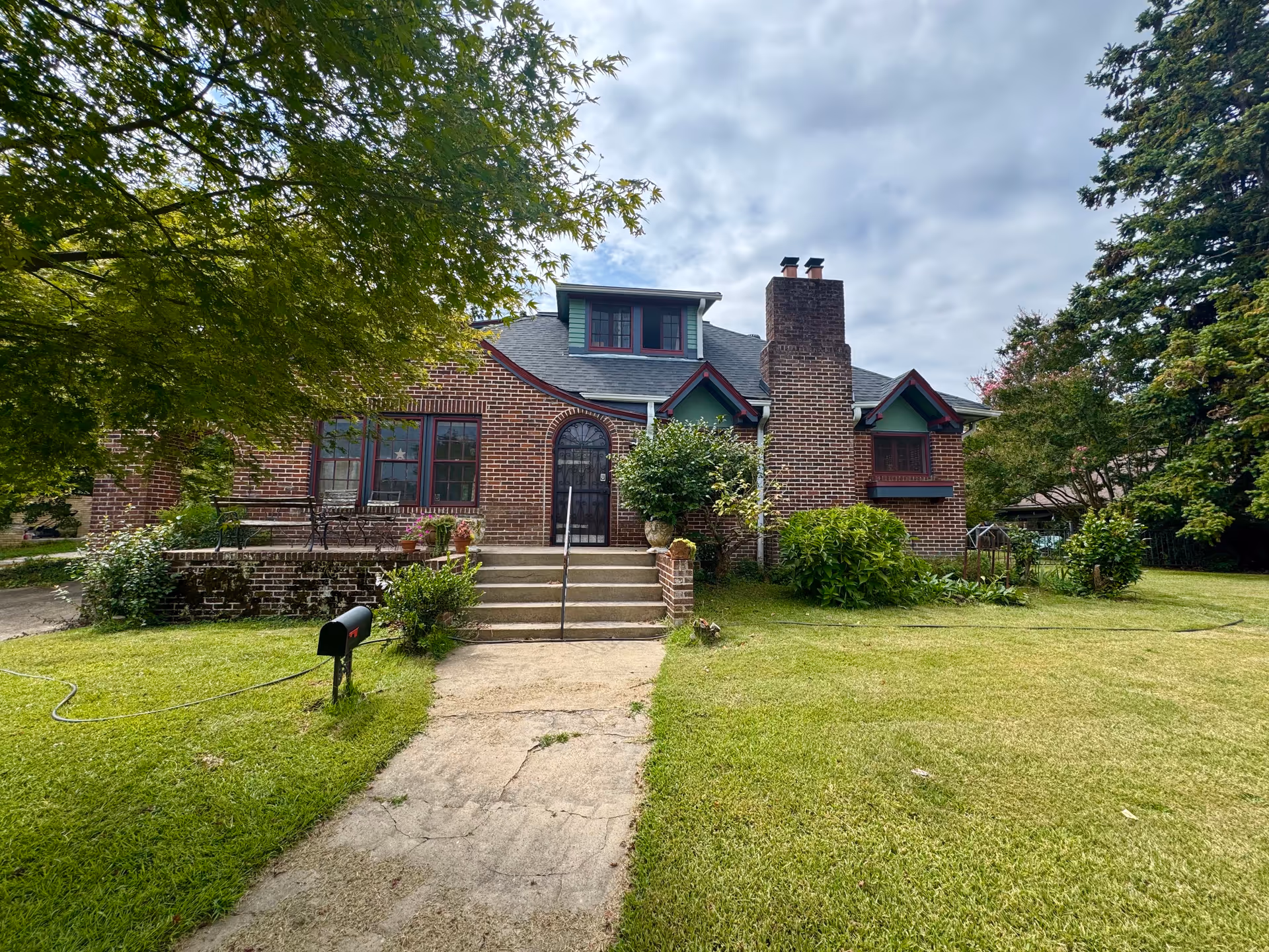 Brick-faced house with a central door, steps, and a green lawn.