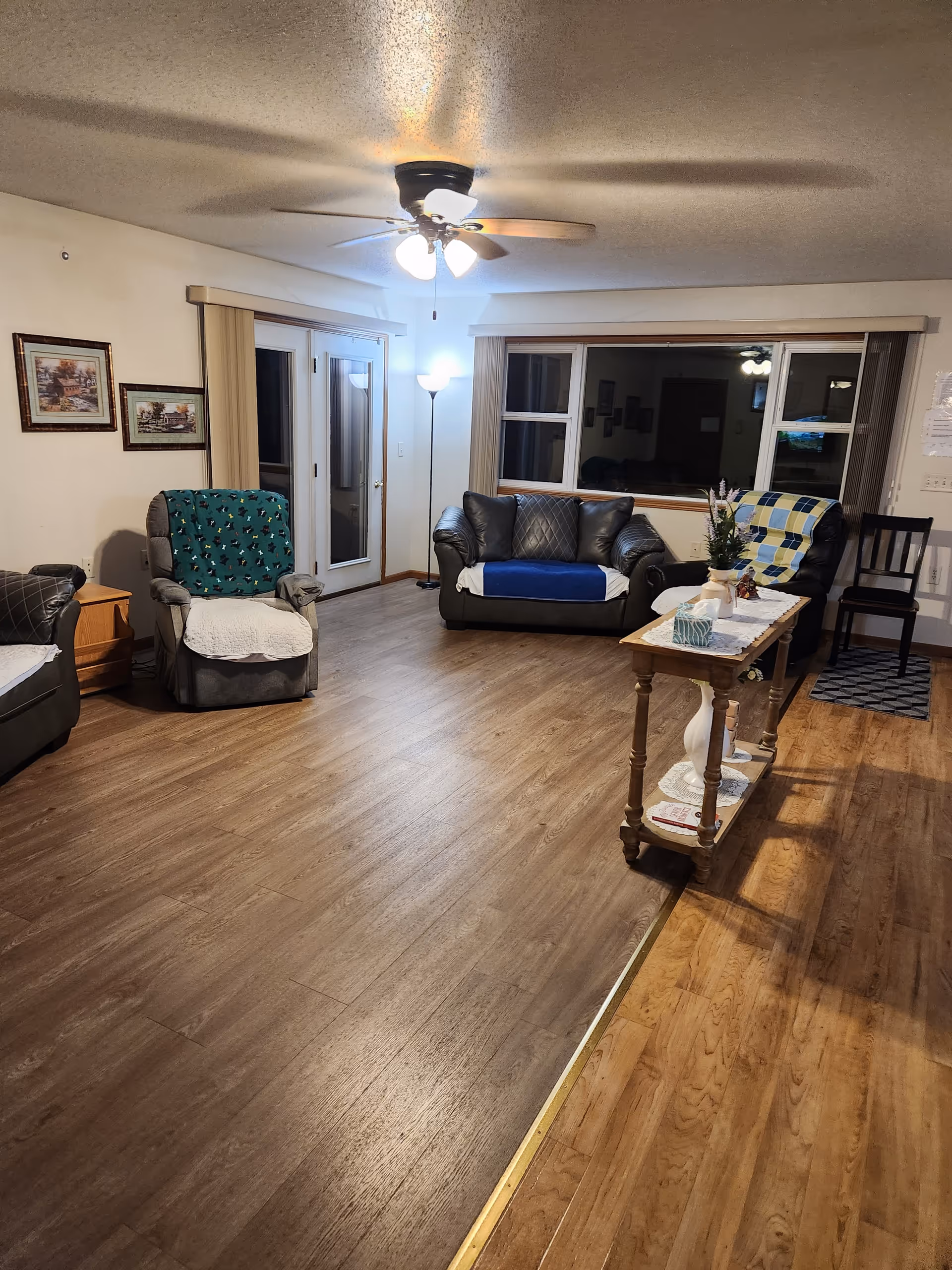 Cozy living room in a senior facility with couches, chairs, a coffee table, and a lamp.