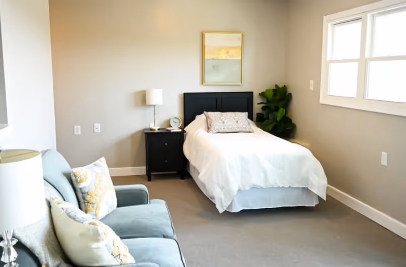 A tidy bedroom in a senior living facility with a bed and sofa.
