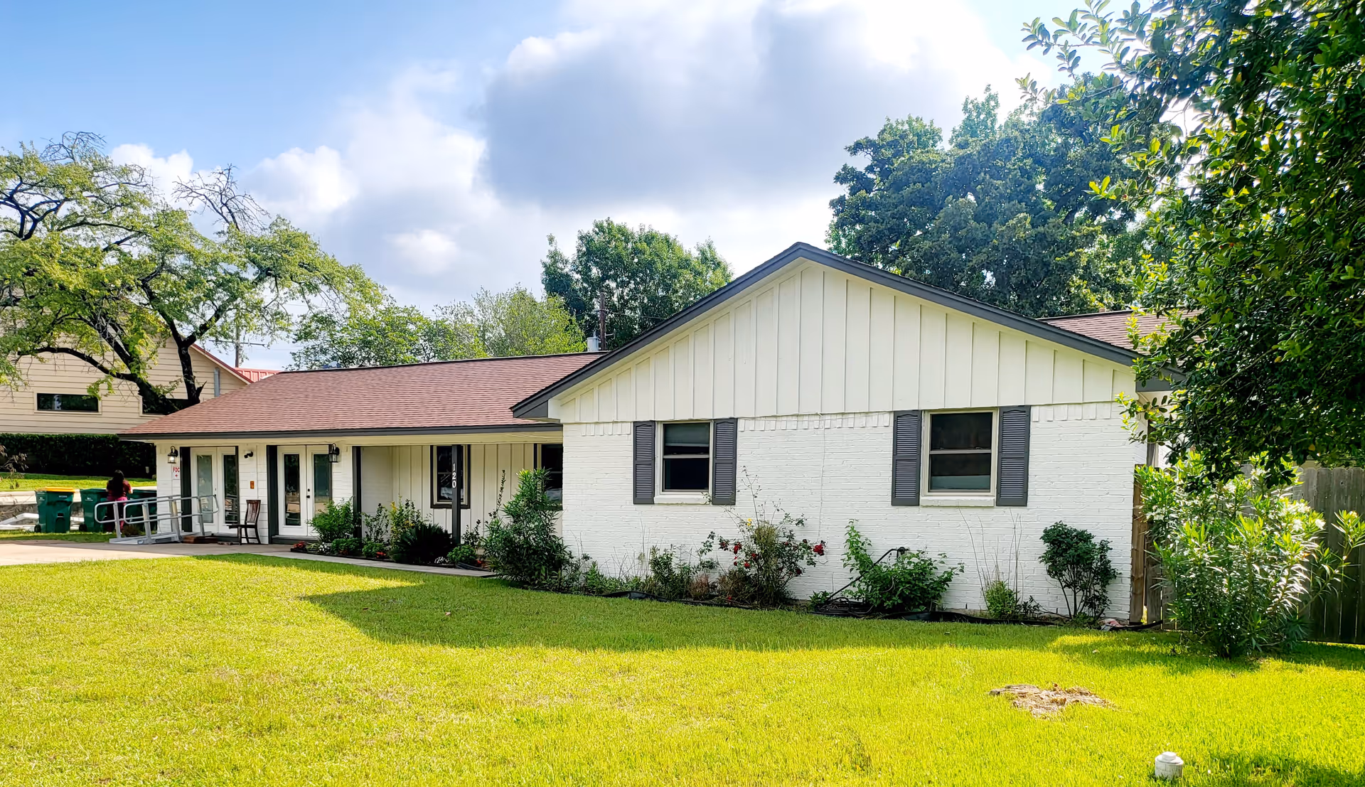White, single-story building with a ramp, lawn, and shrubs in front.