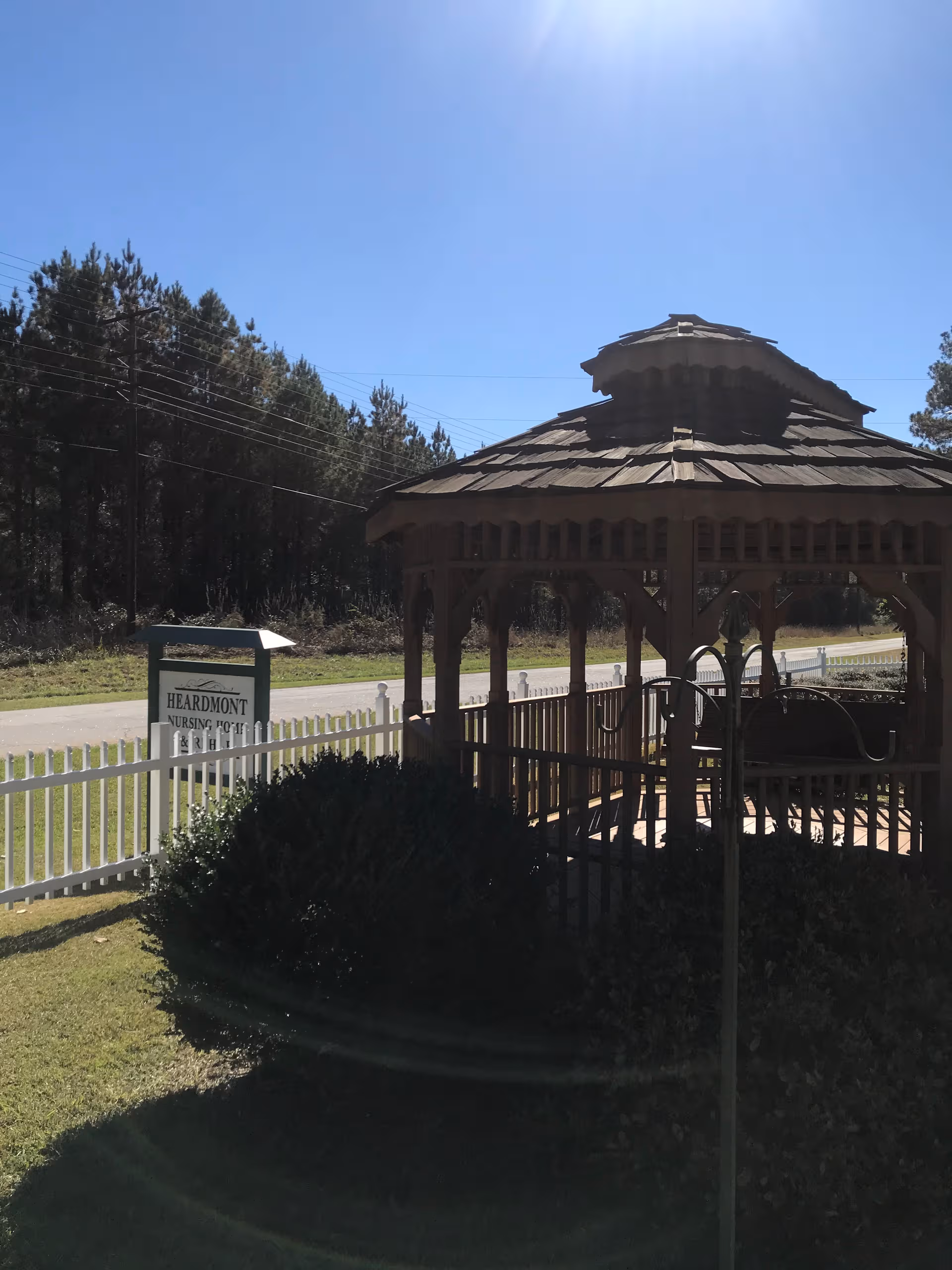 Wooden gazebo beside a white picket fence and a Heardmont Nursing Home sign.
