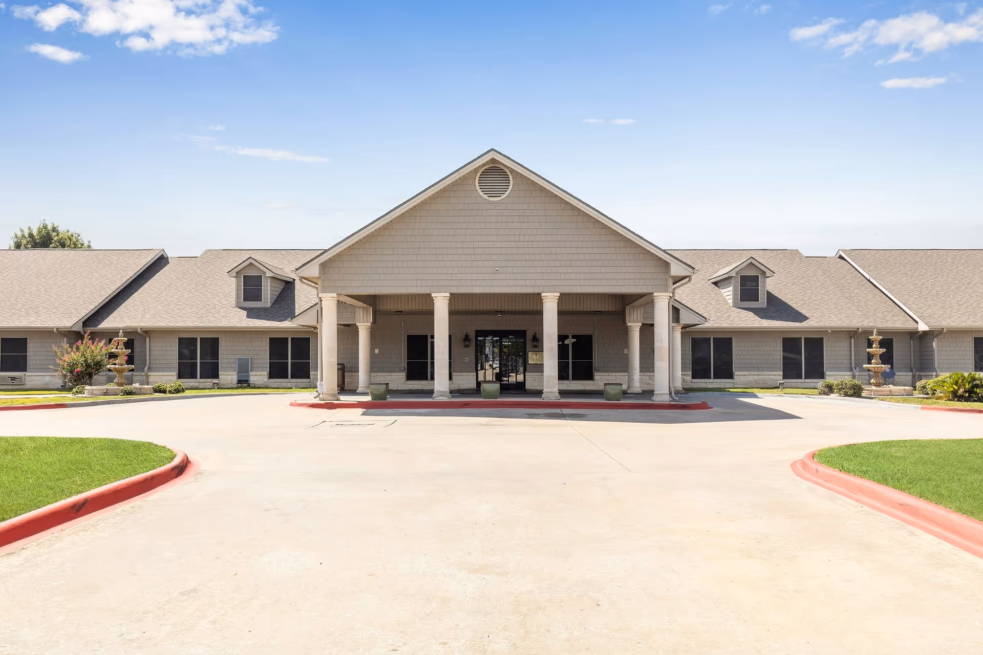 Exterior view of a single-story senior living facility with a covered entrance and driveway.