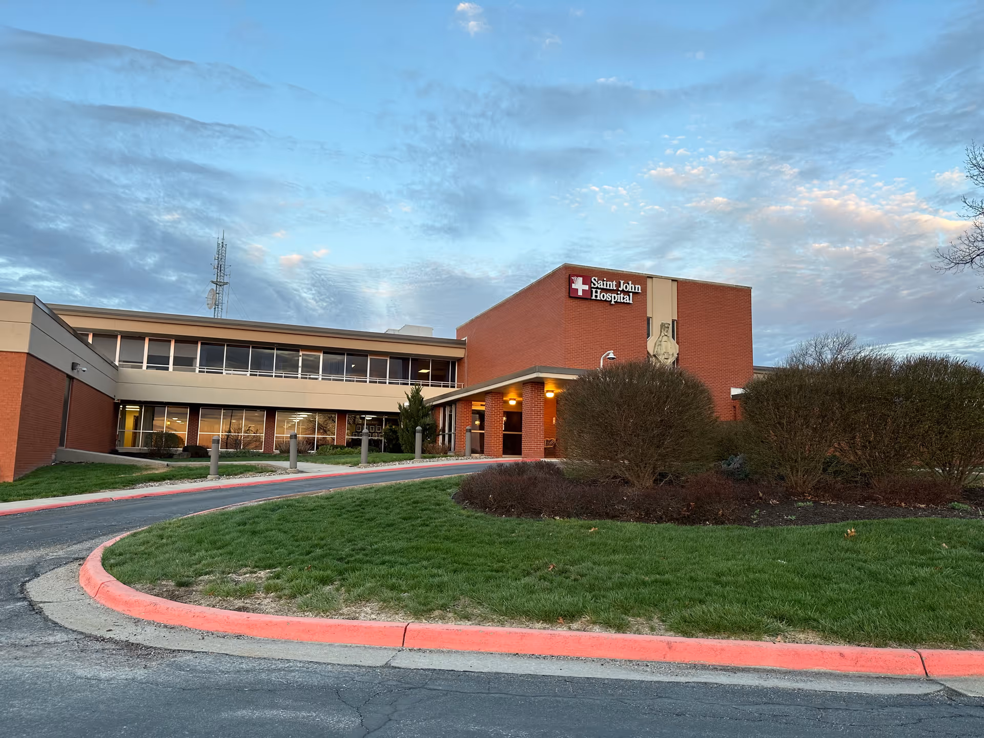 Exterior view of Saint John Hospital building with entrance, brick walls, and landscaped surroundings.