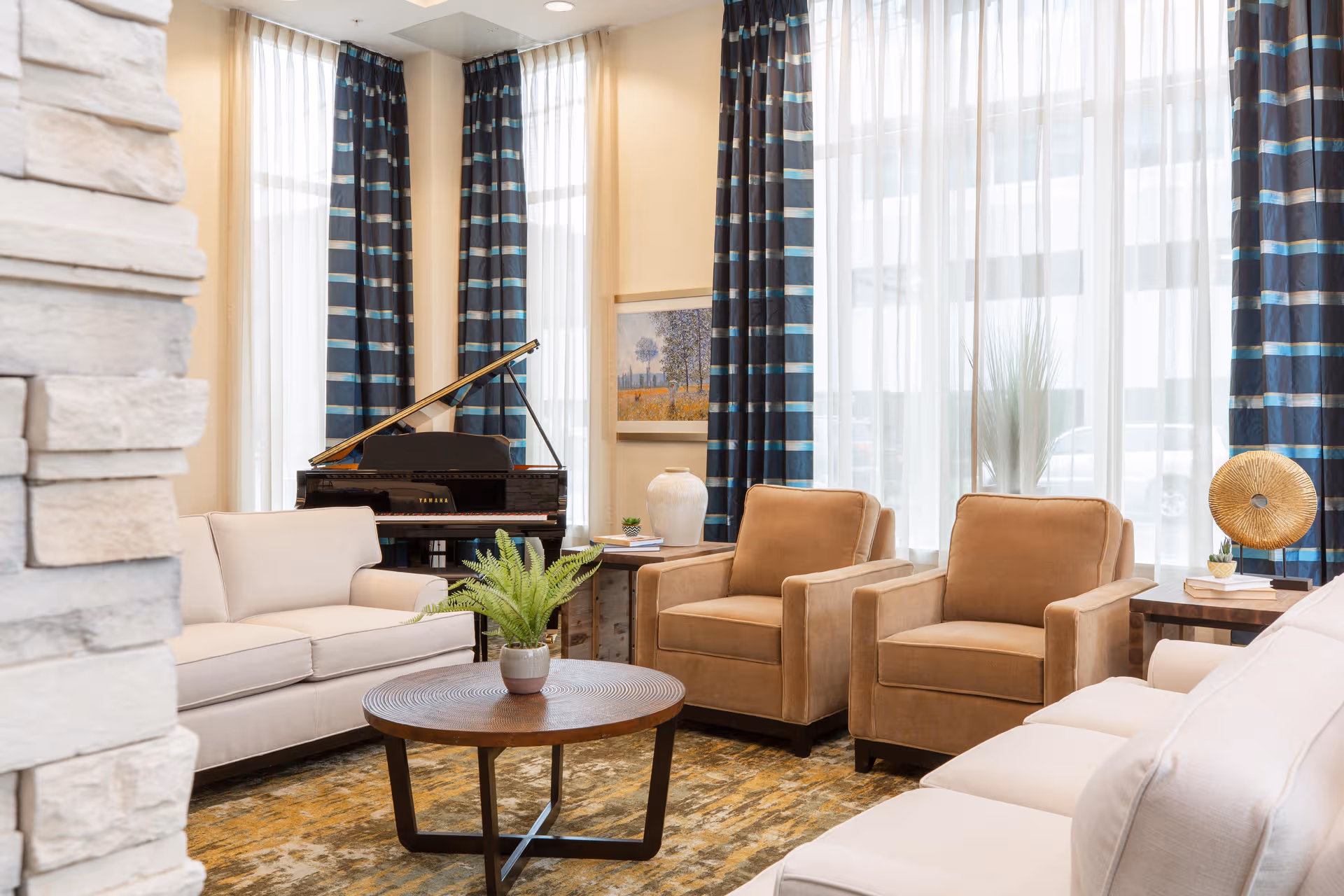 Bright senior living lounge with beige seating, piano, curtains, and a round coffee table.
