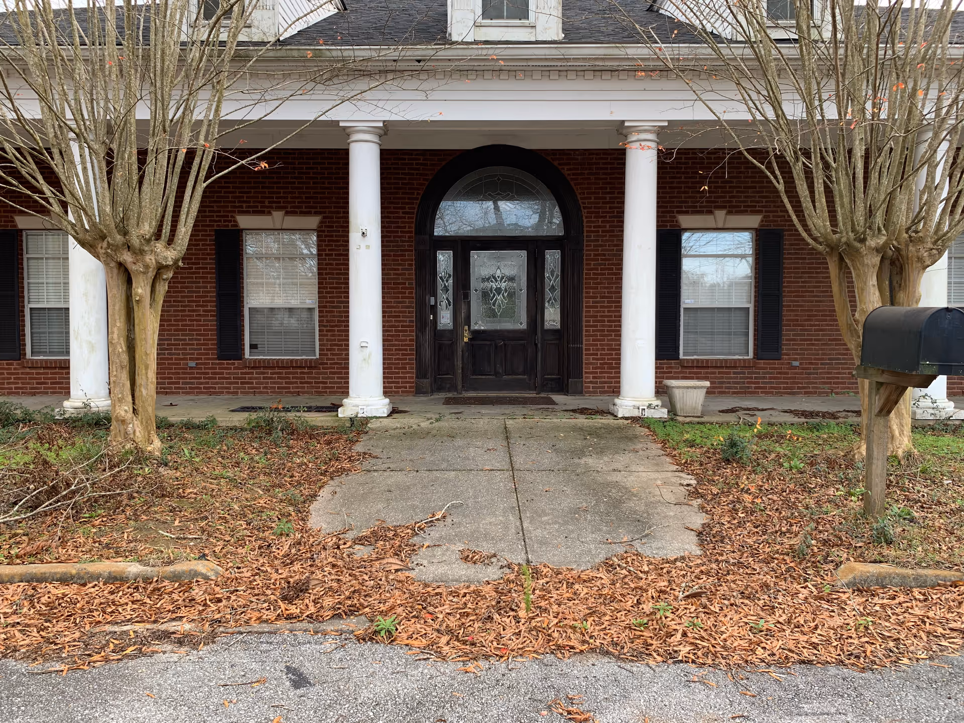 Red brick senior living building with white columns and glass-paneled front entrance.
