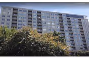 Tall multi-story senior living building with many windows, partly obscured by trees.