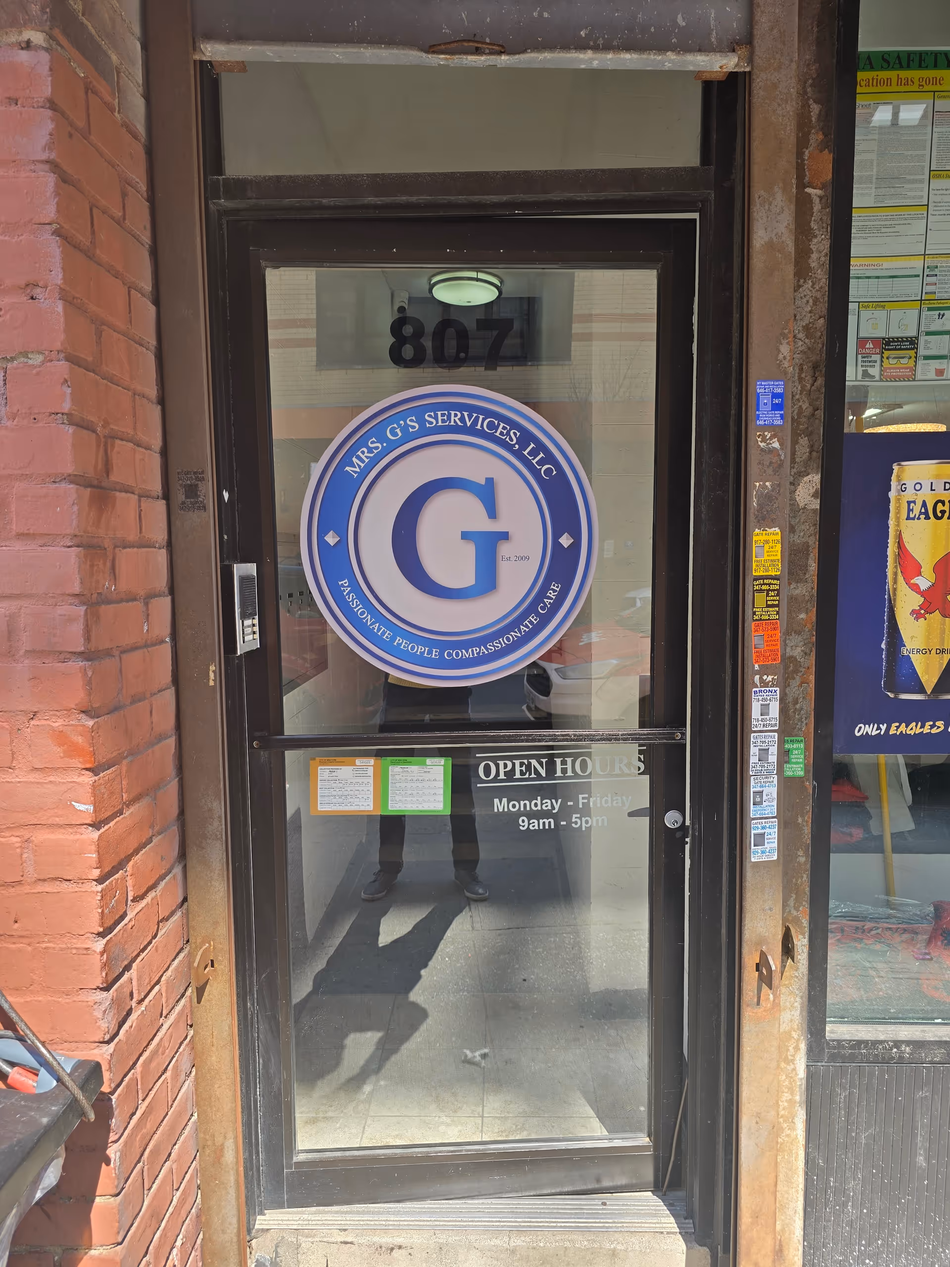 Storefront door features circular blue Mrs. G's Services sign and open hours.