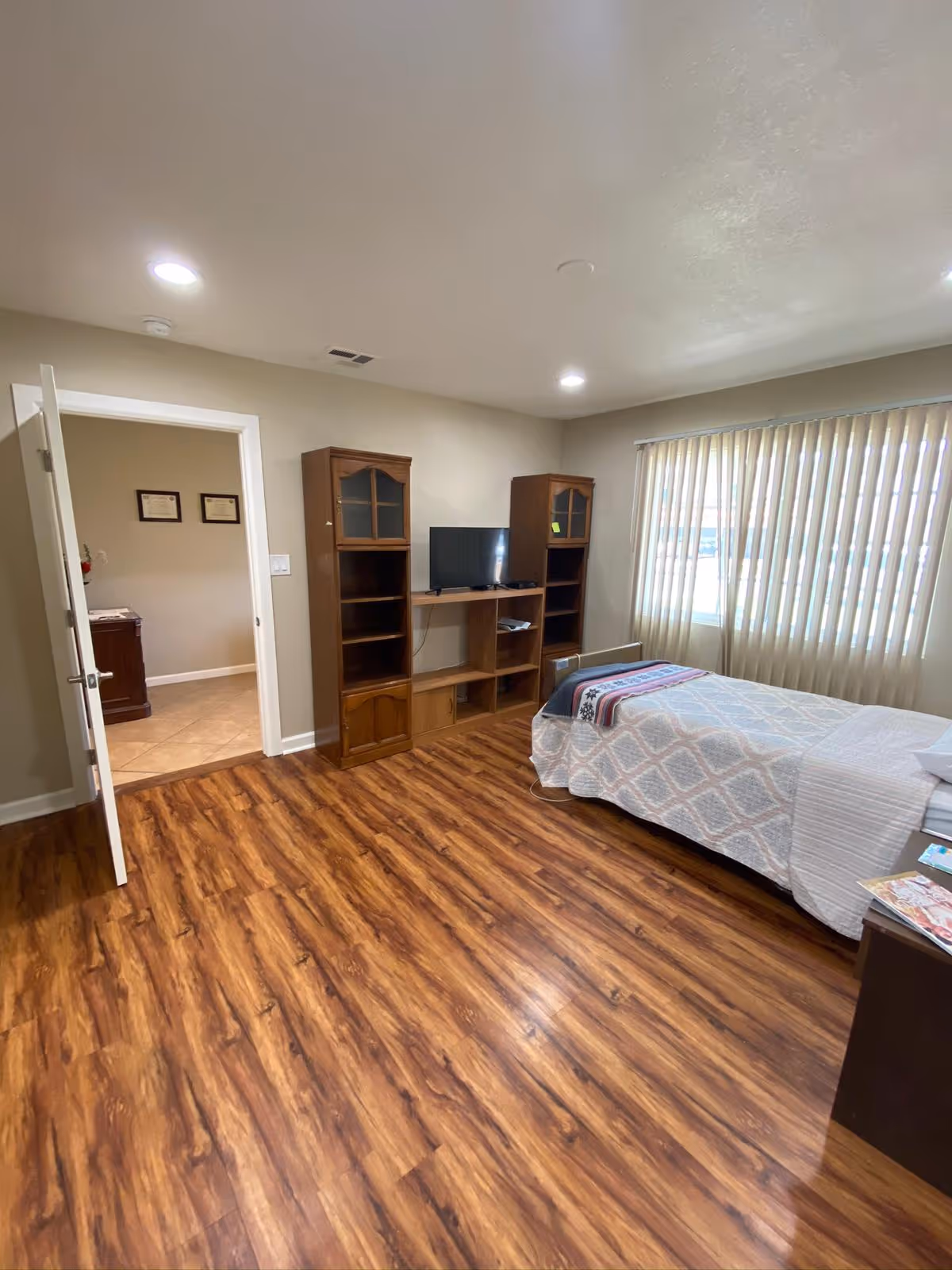 A cozy senior living bedroom with a bed, TV stand, and wooden shelving unit.