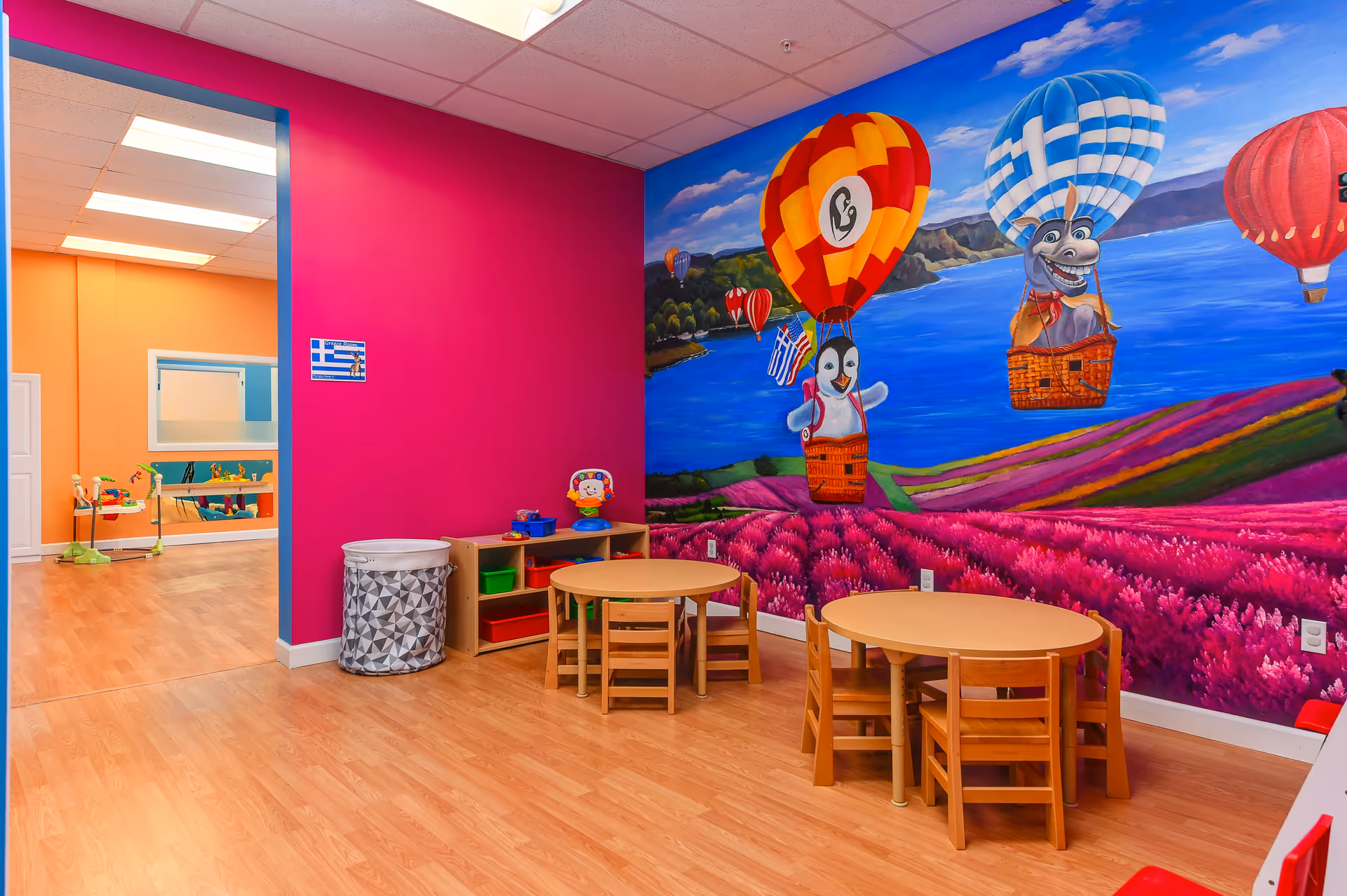 Bright indoor playroom with colorful mural, small tables, and kid-sized chairs.