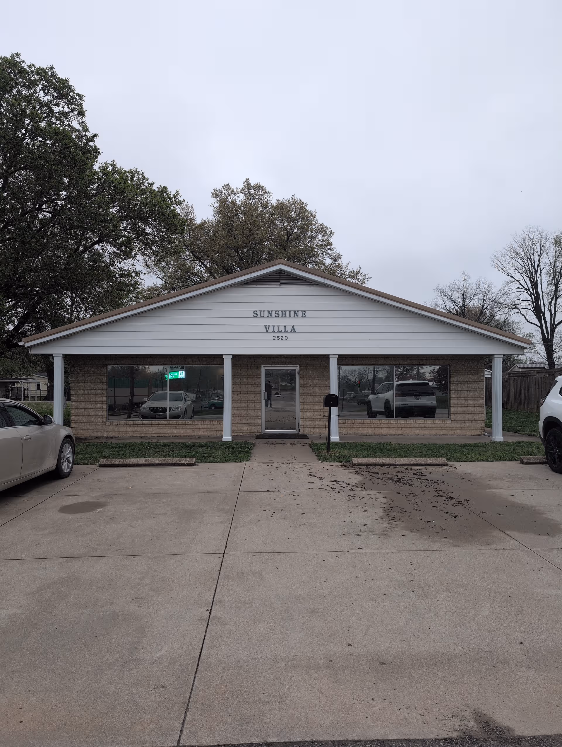 Front view of Sunshine Villa facility with brick exterior, glass windows, and parked cars.