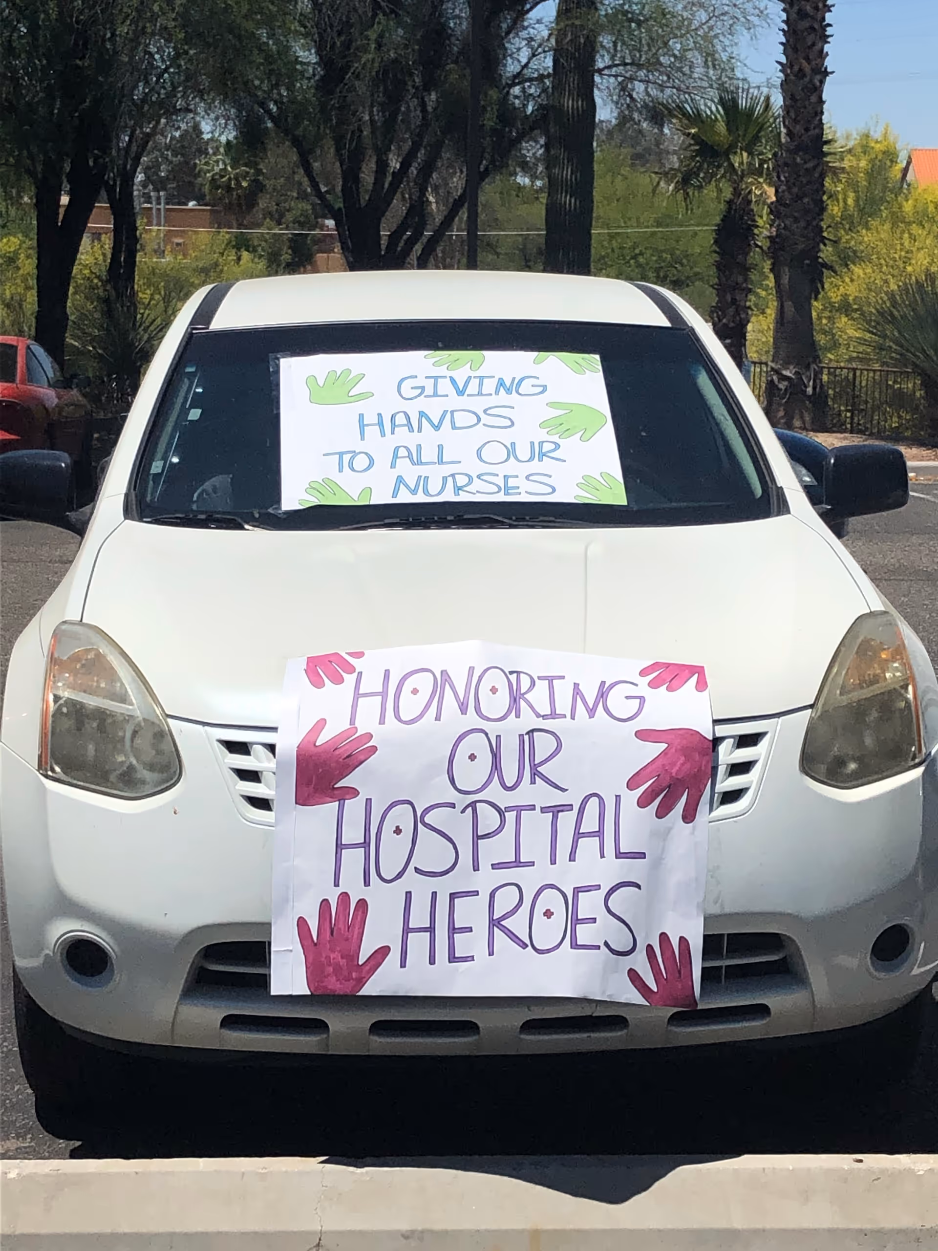 White car with two handmade signs praising nurses and hospital heroes.