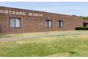 Brick exterior of Orchard Manor facility with grassy foreground and small windows.