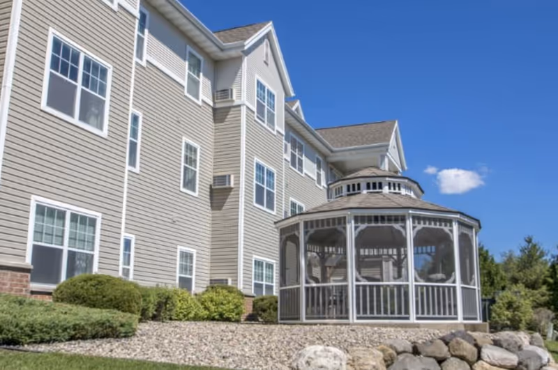 Senior living facility exterior with beige siding and a glass-paneled gazebo