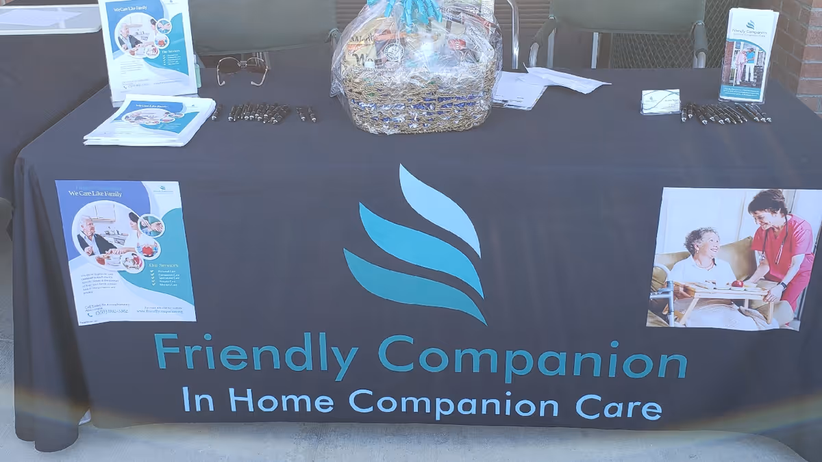 Promotional outdoor table with Friendly Companion banner, brochures, and a gift basket.