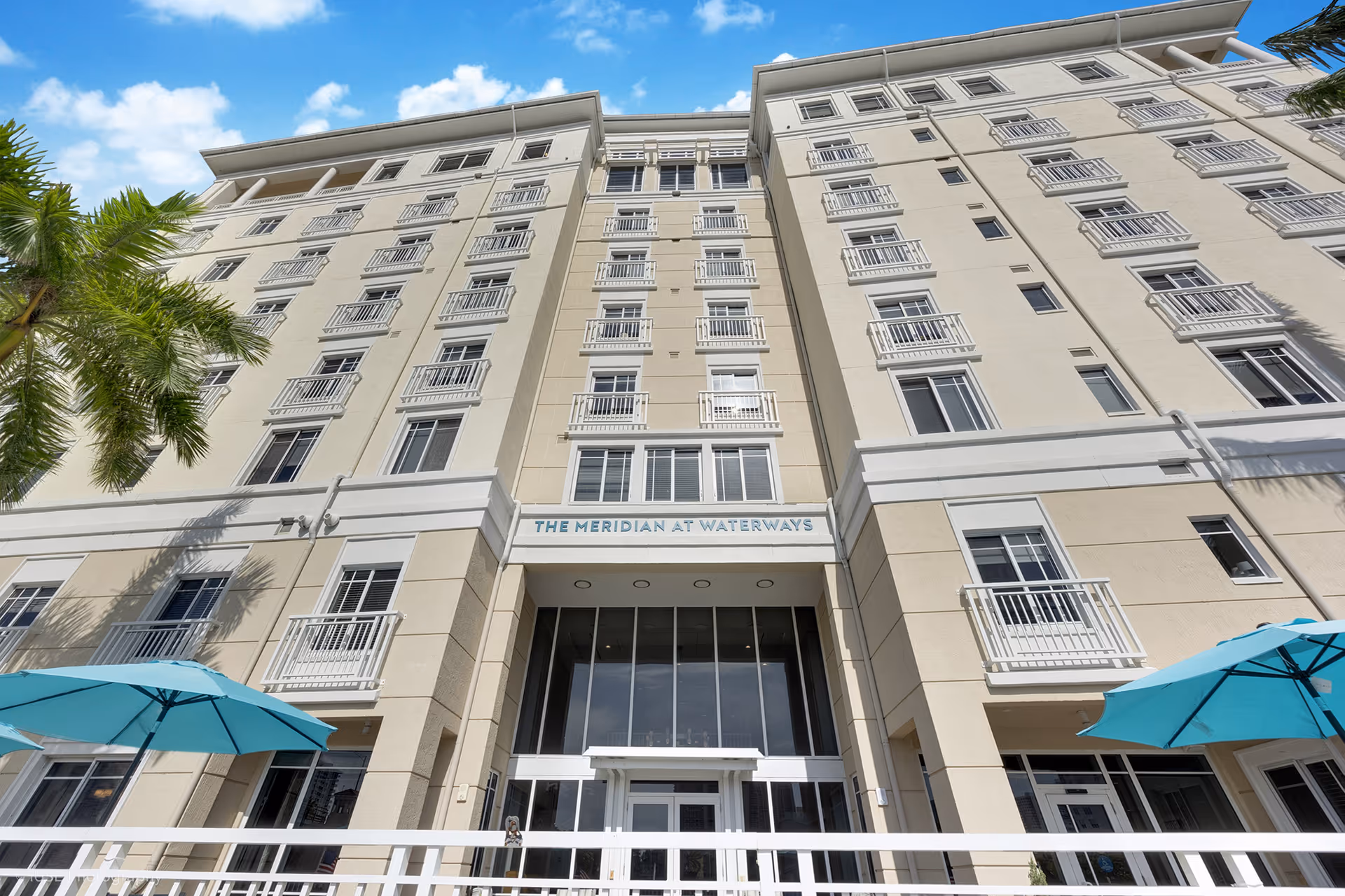 Tall beige senior living building with balconies and a glass entrance labeled The Meridian at Waterways.