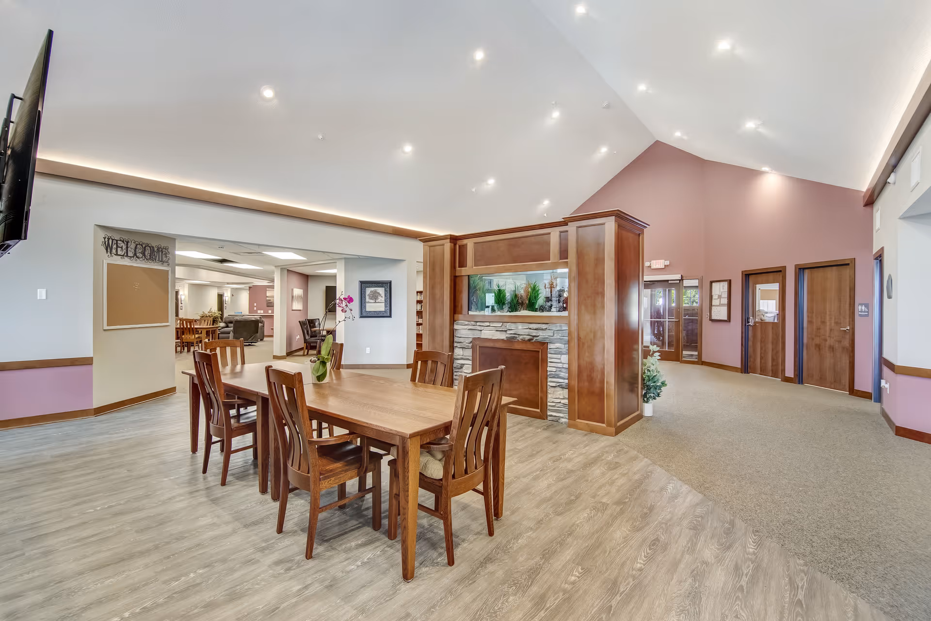 Bright communal living area with a wooden dining table, chairs, and a stone fireplace.