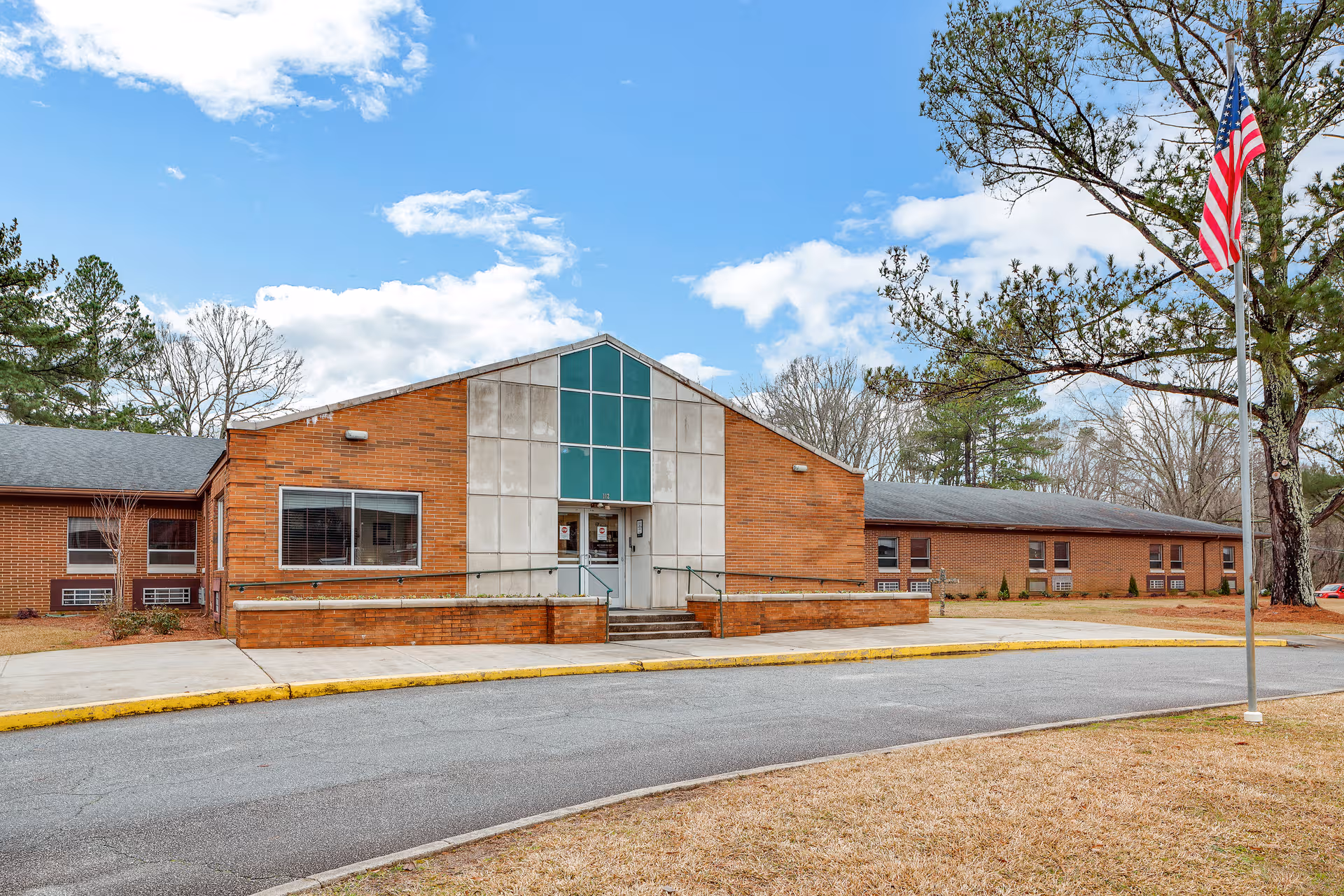 Exterior view of PruittHealth Washington: brick building with glass entrance, ramp, flag, and trees.