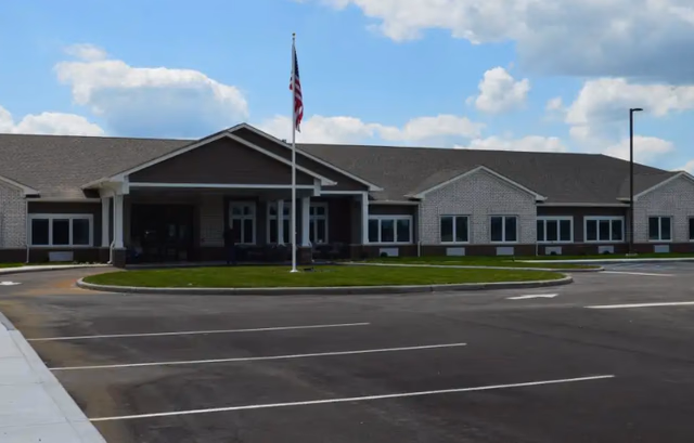 Front view of Autumn Trace Madison Assisted Living, a single-story brick facility with flagpole and parking.