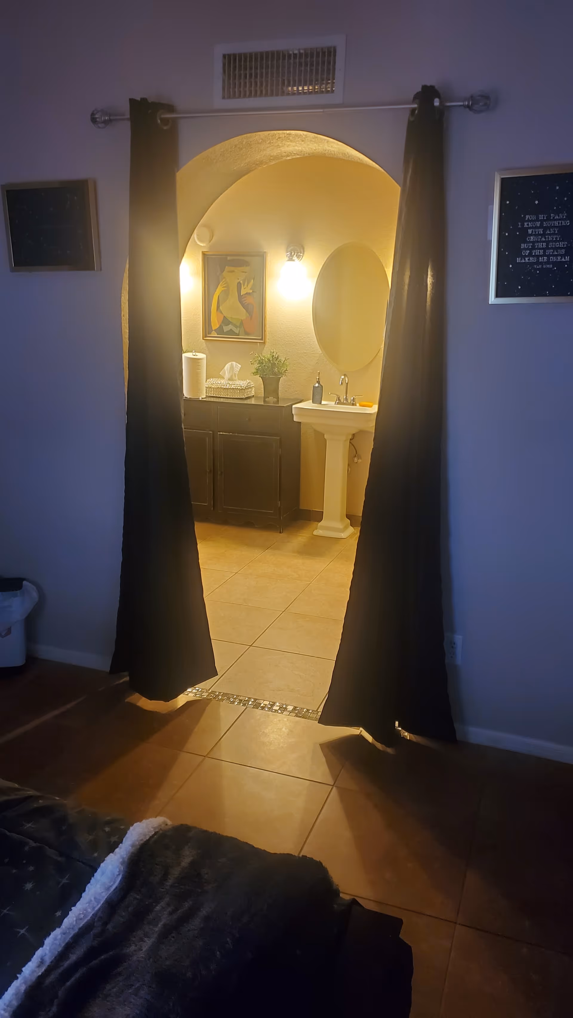A bedroom doorway with black curtains reveals a lit bathroom with sink, mirror, and decor.