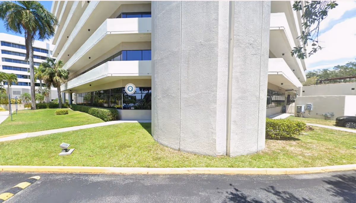 Exterior view of a multi-story senior living building with lawn, palm trees, and curved concrete pillar.
