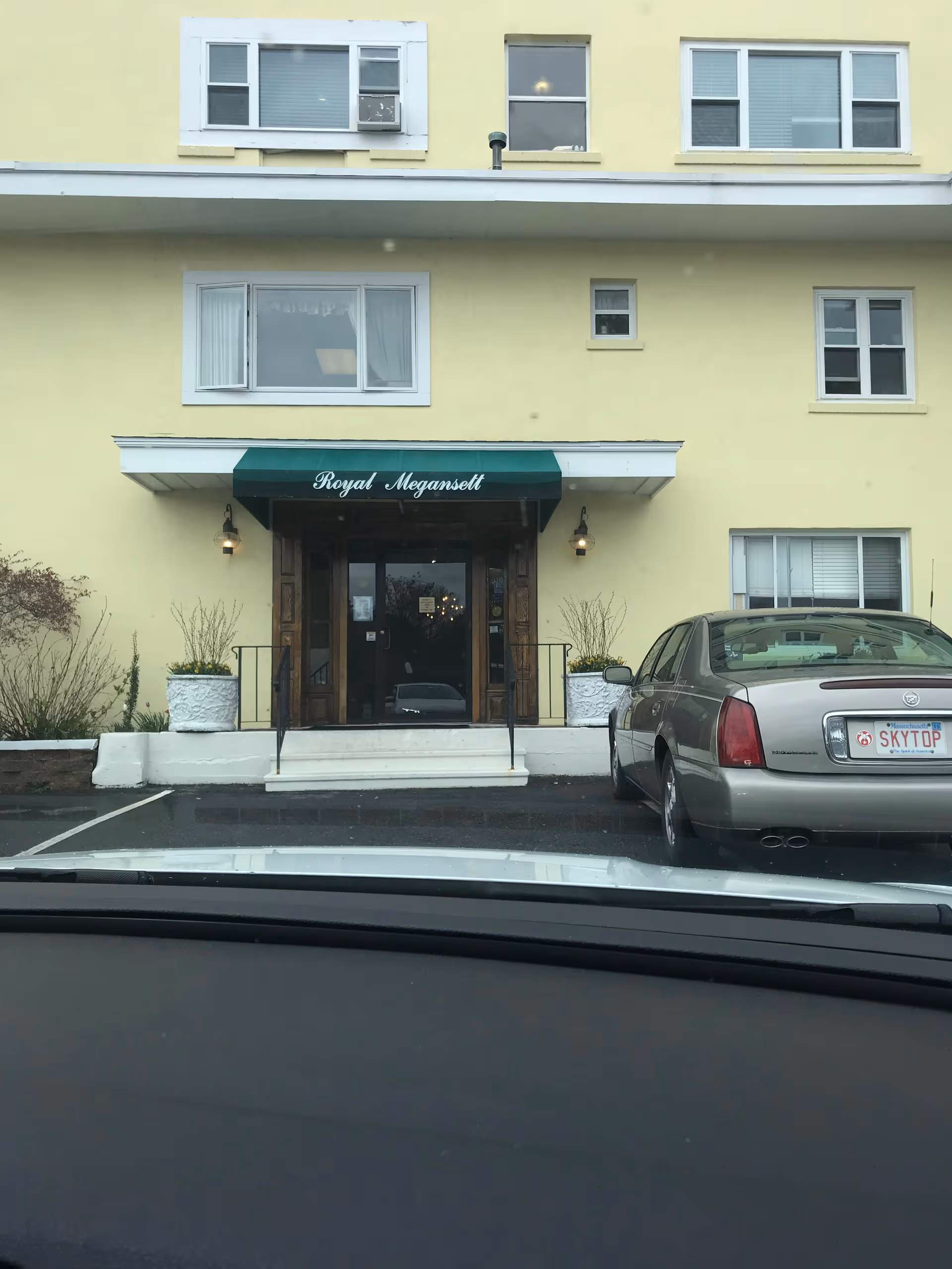 Yellow three-story building with a green awning over glass doors reading 'Royal Megansett', cars parked.