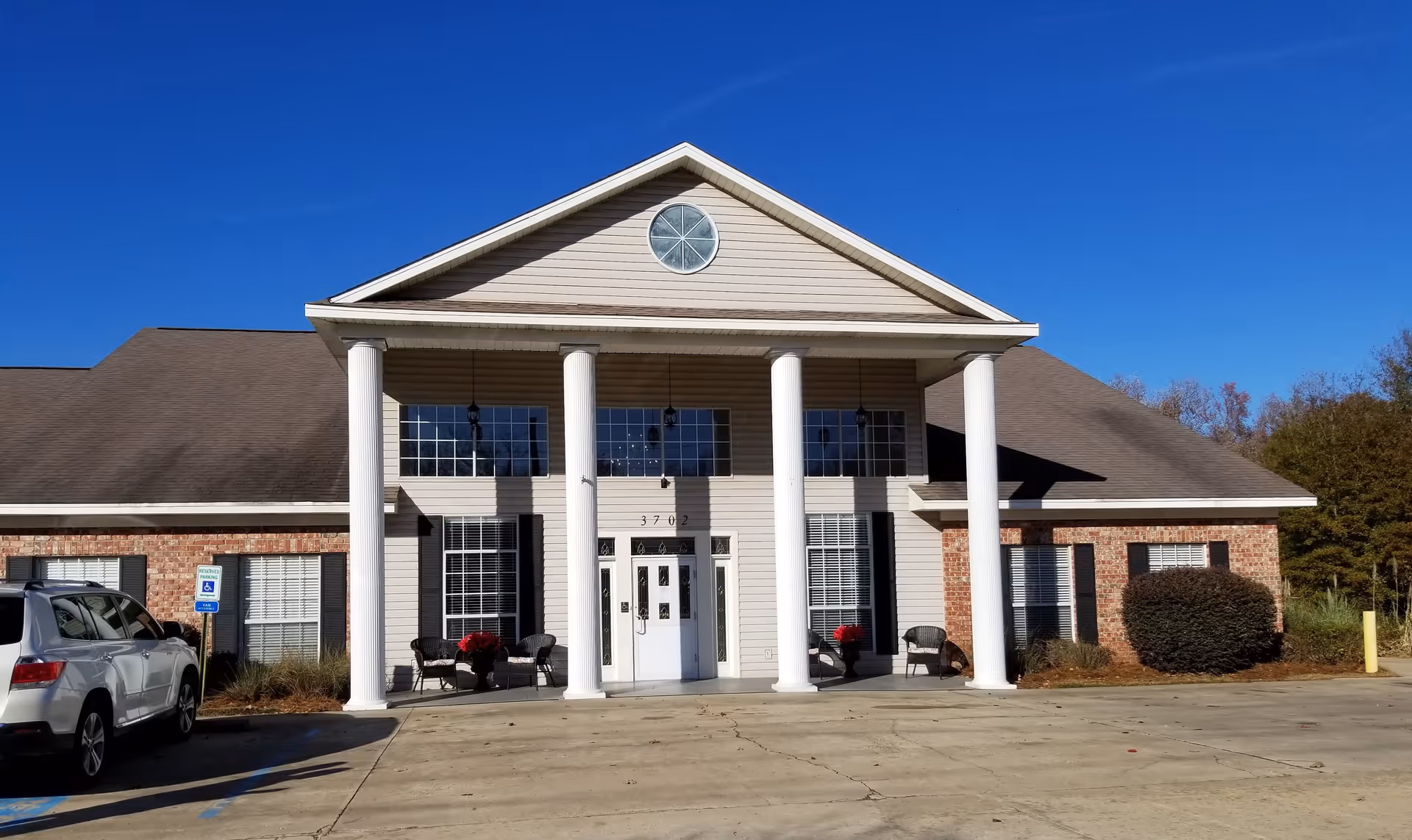 Front entrance of a one-story brick and siding senior living building with four white columns, double doors, and a parking area.