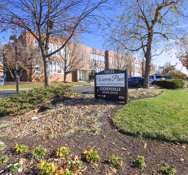 Exterior of Warren Place Senior Apartments with sign, trees, and landscaped front yard.