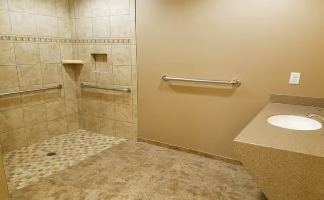 Accessible bathroom with beige tiled walls, walk-in shower, grab bars, and a vanity sink.