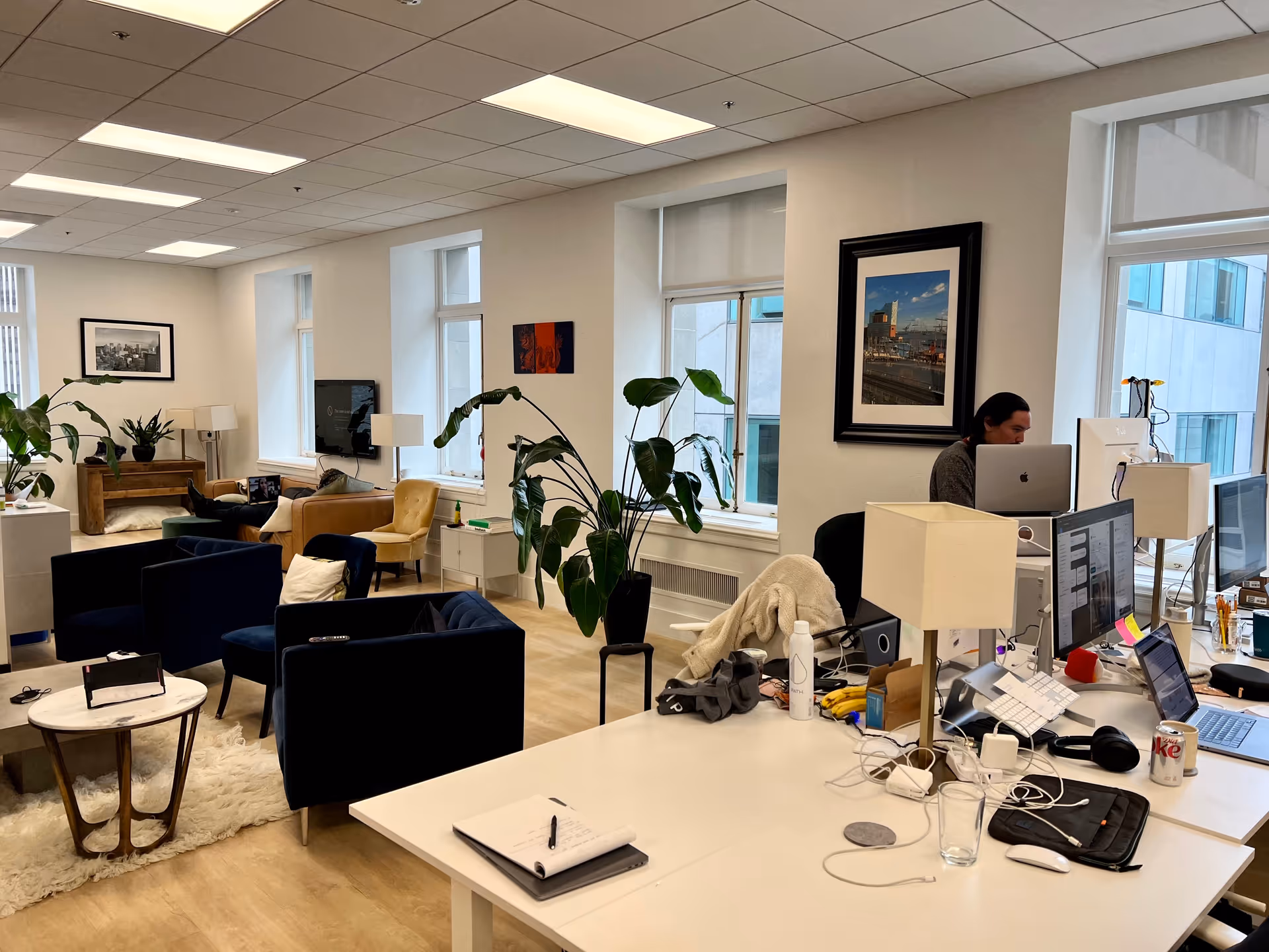 Open lounge and workspace with desks, plants, and seating in a bright facility common area.