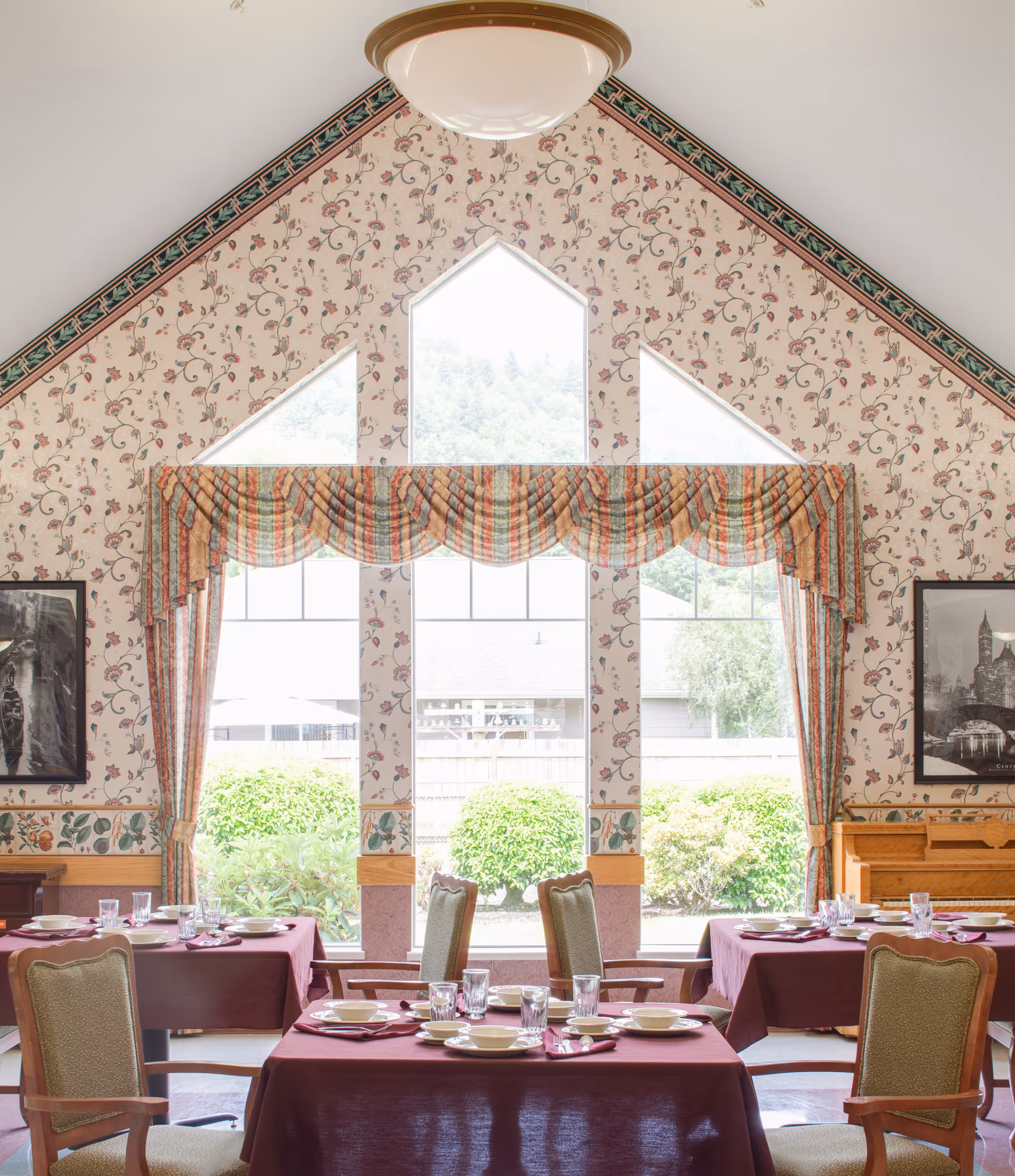 Dining room in a senior living facility with maroon tablecloths and arched windows.
