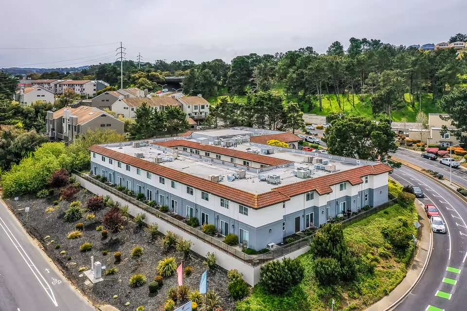 Aerial view of a two-story senior living complex with red-tiled roofs surrounded by roads and greenery.