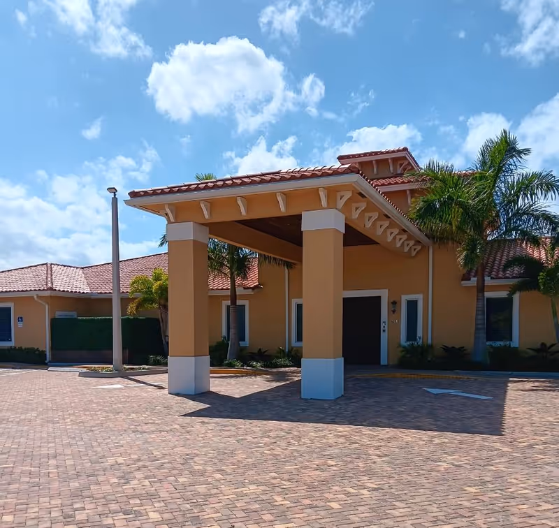 A beige senior living facility entrance with a porte-cochère and palm trees.