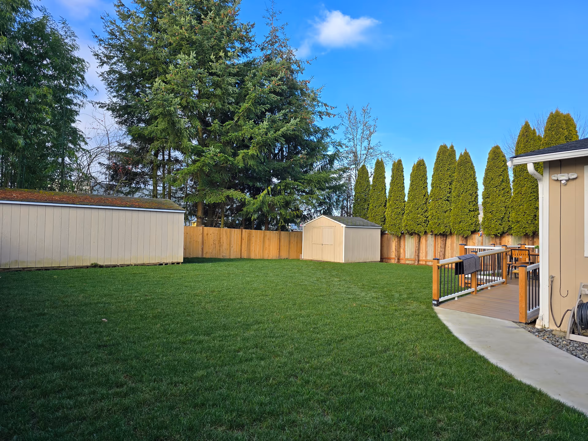 Spacious backyard with green lawn, wooden fence, shed, and outdoor deck with seating.
