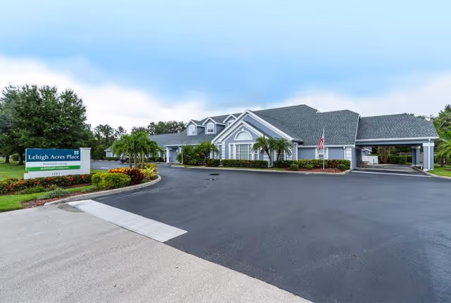 Front exterior of a single-story assisted living building with a driveway, landscaped grounds, and a Lehigh Acres Place sign.