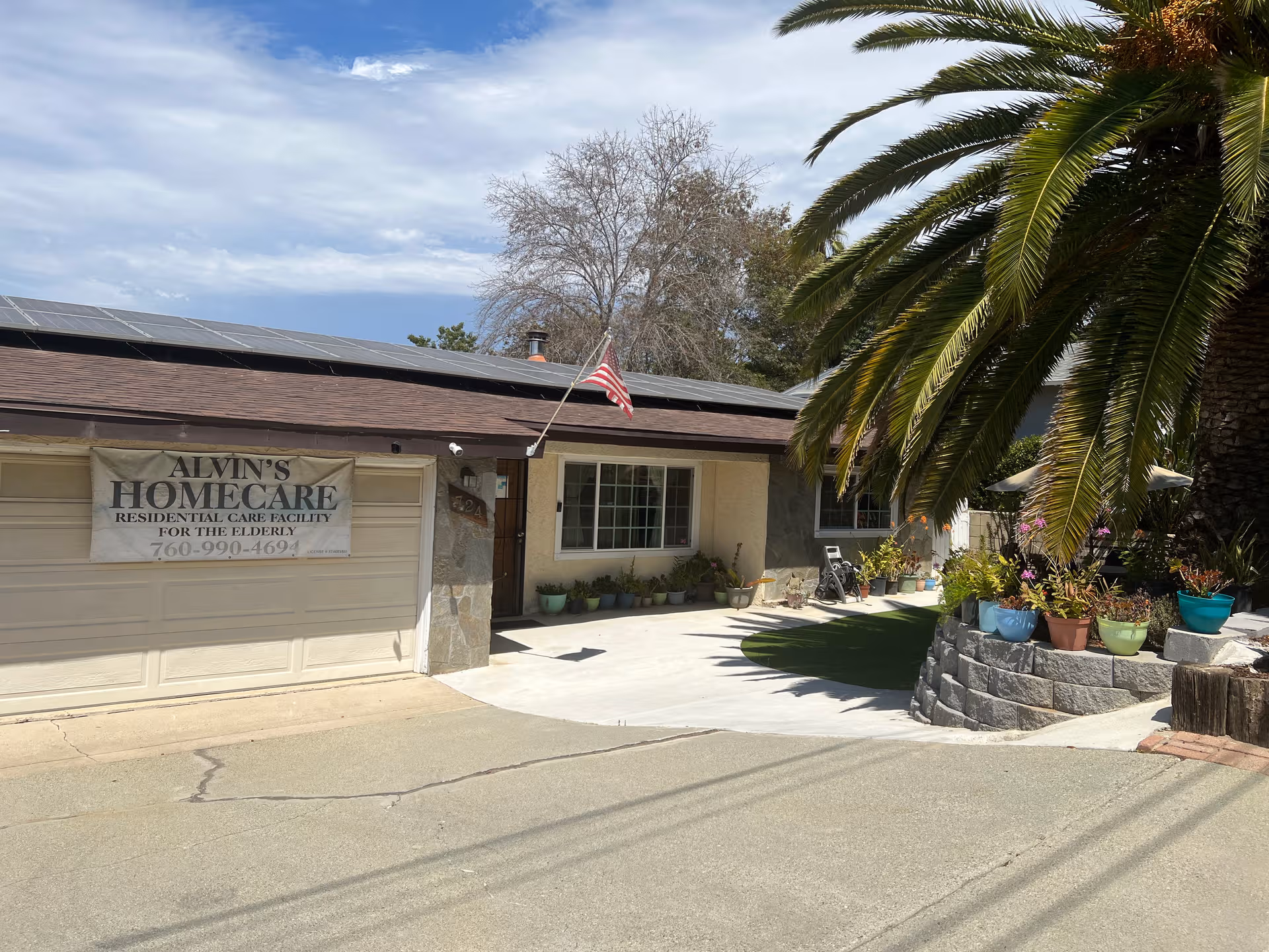 Front exterior of Alvin's Homecare facility with entrance, palm trees, and decorative potted plants.