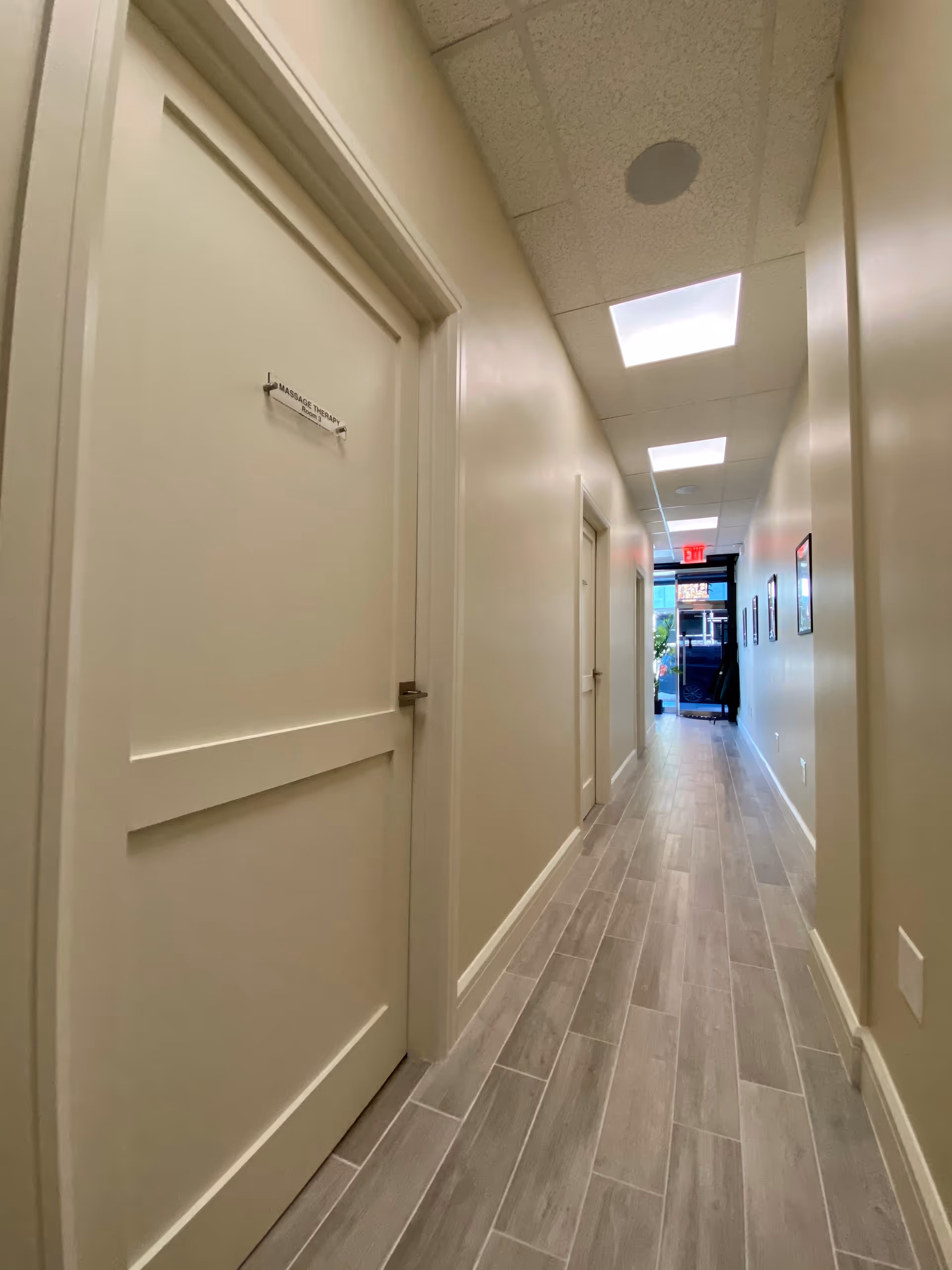 Narrow beige hallway in a senior care facility with closed doors, a sign, and ceiling lights.