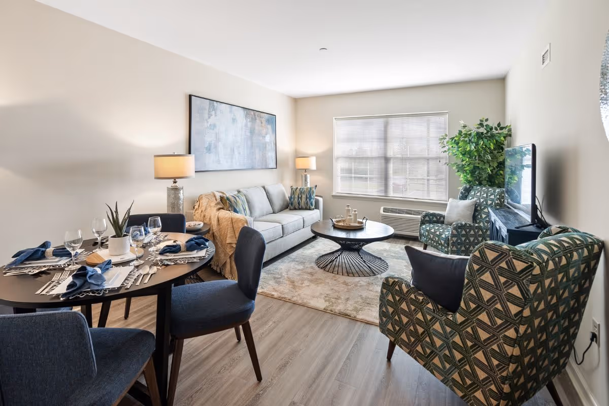 Bright senior living room with a sofa, armchairs, TV, and round dining table.