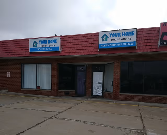Brick storefront with two Your Home Health Agency signs on a red shingled roof.