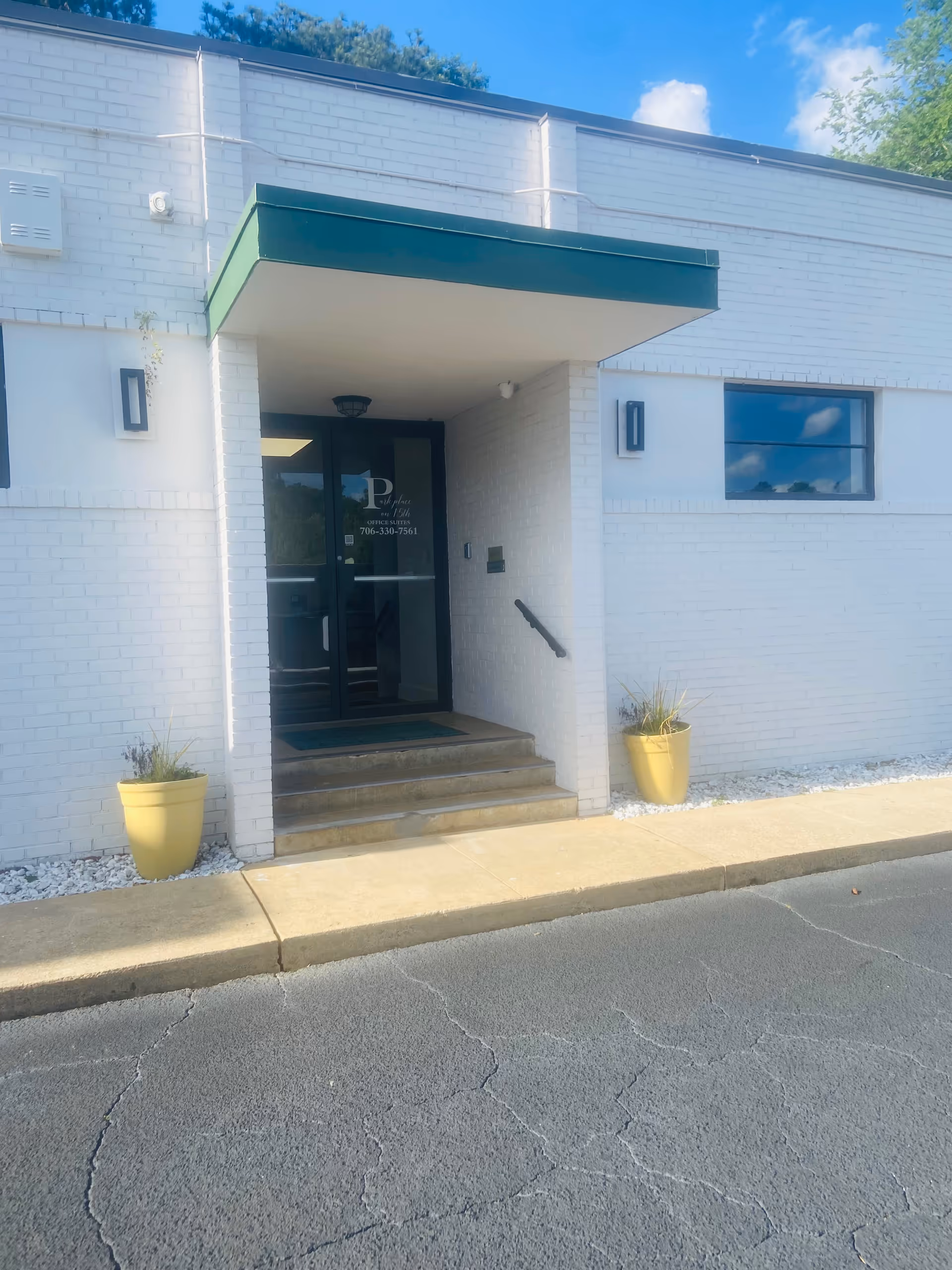 Exterior entrance of a white brick building with glass doors and yellow planters.
