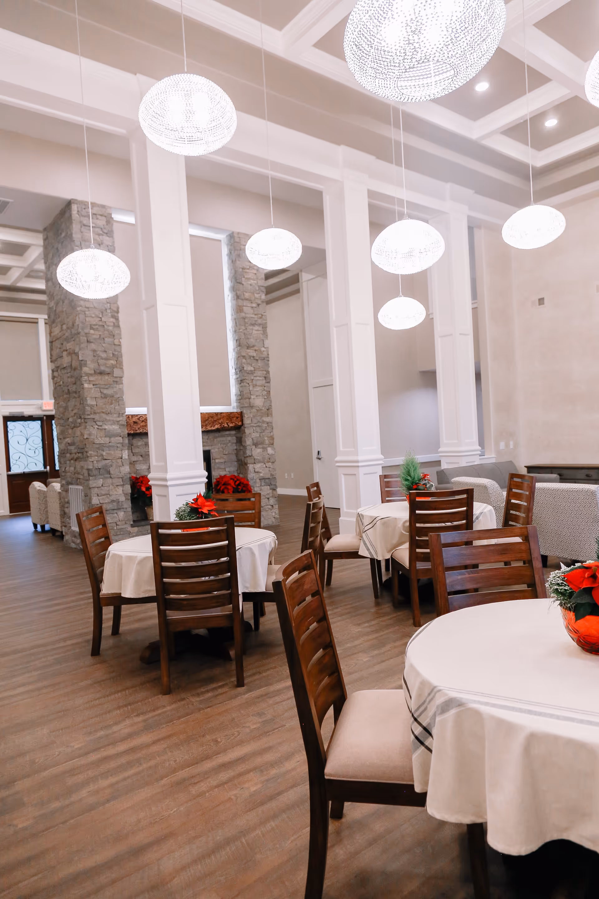 Bright dining room with round tables, white tablecloths, and hanging pendant lights.