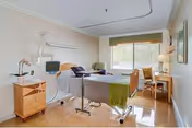 Senior living patient room with adjustable bed, monitor, desk, and window.